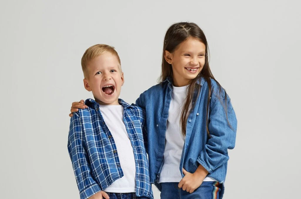 A smiling boy and girl in denim and plaid standing arm in arm